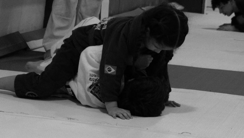 Dos alumnos entrenando jiu-jitsu sobre el tatami, con el profesor al lado